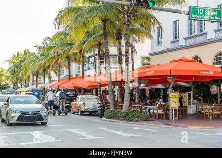 People, cars and outdoor terraces on Ocean Drive at crossing 10th Street in South Beach district of Miami Beach, Florida, USA Stock Photo