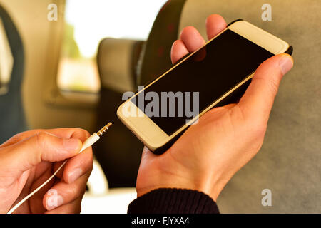 closeup of a young caucasian man plugging the earphones in his smartphone in a train or a subway Stock Photo