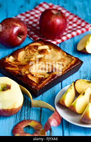 closeup of an apple cake and some red apples on a blue rustic wooden table Stock Photo
