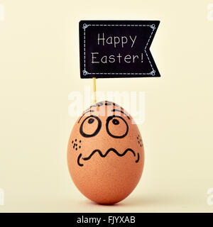a brown egg ornamented with a funny face with a black flag-shaped signboard with the text happy easter, on an off-white backgrou Stock Photo