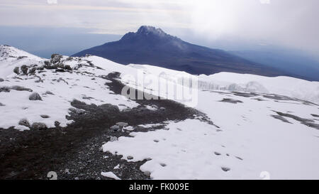 The trail from Stella Point to Uhuru Peak at the summit of Mount Kilimanjaro, and Mount Meru in the background. Stock Photo