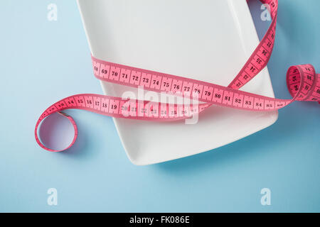 Empty plate wrapped in tape measure on blue background Stock Photo
