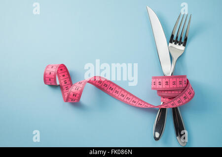 Knife and fork wrapped in tape measure on blue background Stock Photo