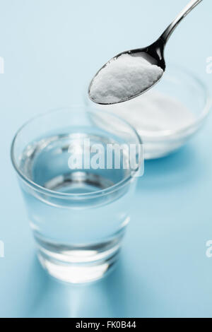 Spoon of baking soda above a glass of water on blue background Stock Photo