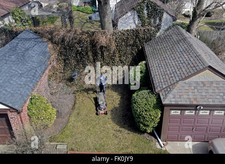 A view from above of a gardener mowing the lawn at a suburban home in Queens, New York Stock Photo