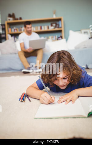 Boy writing in book while father working in background Stock Photo