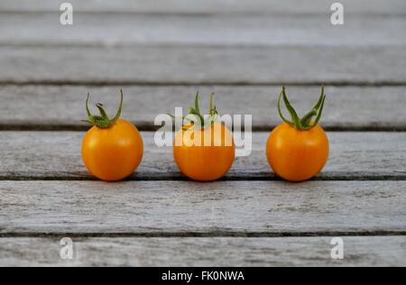 Three Sungold yellow cherry tomatoes in a row on a wooden table Stock Photo