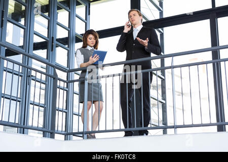 Businessman talking on smartphone and businesswoman using digital tablet Stock Photo