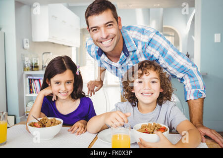 Happy man standing by children having breakfast Stock Photo