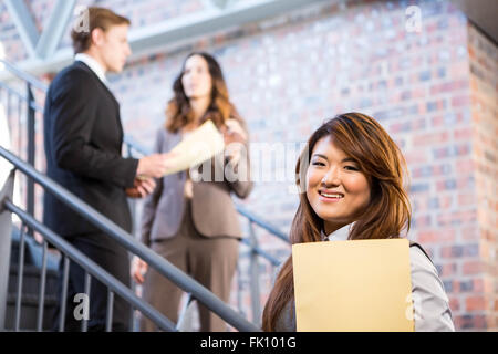 Businesswoman standing near staircase with documents Stock Photo