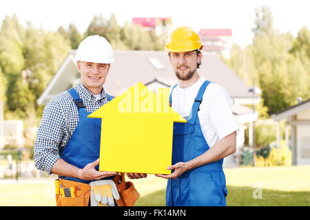 Happy smiling workers in hardhats holding house model Stock Photo