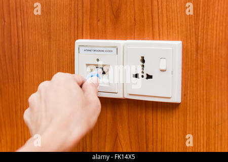 Hand plugging in internet LAN cable into socket. Technology and communication concepts. Stock Photo