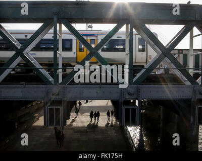 Hungerford railway bridge with a train and commuters below Stock Photo