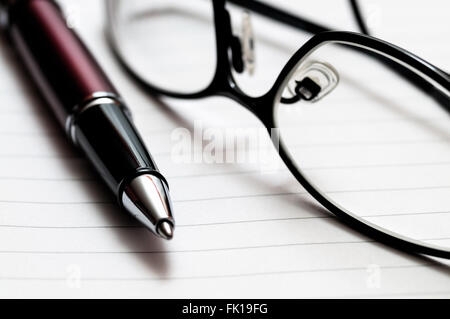 Picture of a close-up of a red and black pen and prescription glasses on lined notebook paper. Stock Photo