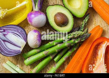 Close up view showing sliced fresh vegetables on a wooden table, flatly, asparagus avocado, bell peppers, onion Stock Photo