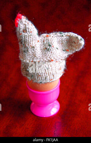 Boiled egg in pink egg cup with woolen hen cosy Stock Photo