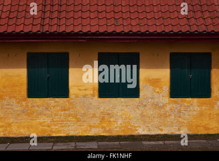 Three green wood shutters in a yellow plastered brick facade of an old house with red roof tiles Stock Photo
