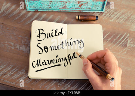 Retro effect and toned image of a woman hand writing a note with a fountain pen on a notebook. Handwritten text Build Something Meaningful as business concept image Stock Photo
