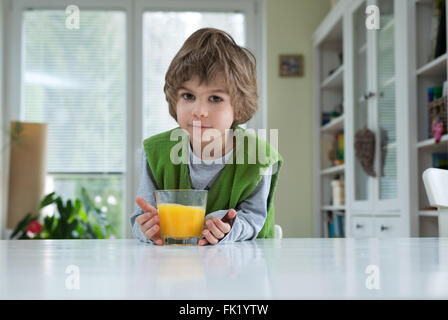 Cute little boy sitting at the table drinking orange juice for breakfast. Healthy lifestyle, nutrition and healthy eating Stock Photo