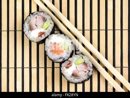Three sushi rolls and chopsticks over bamboo mat Stock Photo