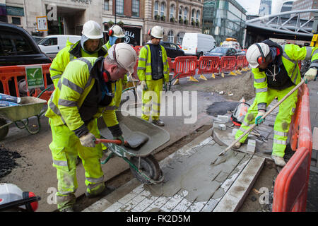 Workmen laying and spreading cement on a pavement and road in London Stock Photo