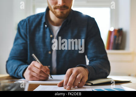 Cropped view of unidentifiable man in blue shirt with hand over paperwork as if to check statistics or plan something important Stock Photo