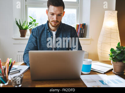 Serious man working on laptop at home office wearing blue shirt Stock Photo