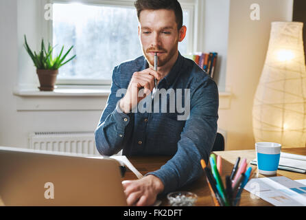 Relaxed business man working on laptop holding a pen in his mouth looking concentrated Stock Photo