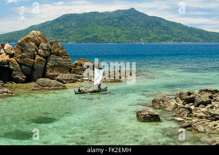 A rocky tropical coast in northern Madagascar with fishermen passing by Stock Photo