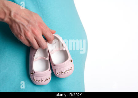 Pregnant belly with hands holding pink baby shoes with room for text Stock Photo