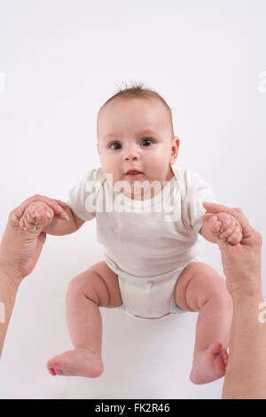 Baby Girl Is Pulling Up Herself At Mothers Hands On White Background Stock Photo