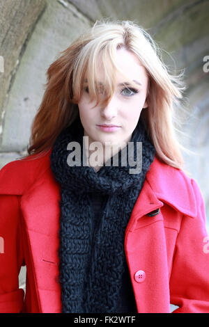 Beautiful young woman with blonde hair wearing red jacket and black scarf on a cold windy day Stock Photo