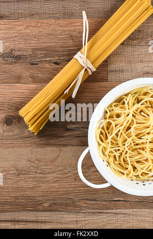 Overhead view of cooked and dried spaghetti. The cooked pasta is in a colander and the raw is tied with raffia. Horizontal on a Stock Photo
