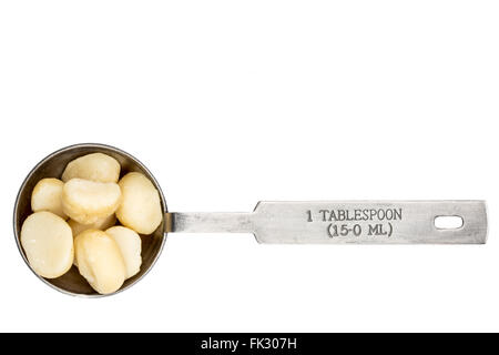 macadamia nuts in a metal measuring tablespoon isolated on white Stock Photo