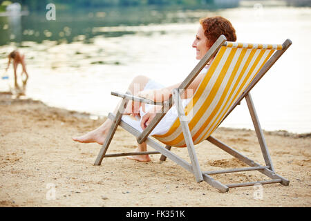 Smiling young woman relaxing on beach in deck chair in summer Stock Photo