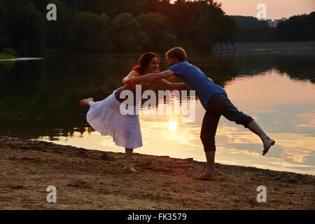 Happy couple doing yoga exercise together on beach at sunset in summer Stock Photo