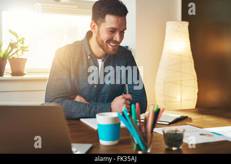 Small business entrepreneur at work in his office at home smiling as he analyses charts and graphs showing performance statistic Stock Photo