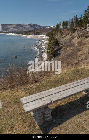 A wooden bench overlooking the Atlantic Ocean in spring on the Cabot Trail in Nova Scotia, east coast Canada. Patches of snow co Stock Photo