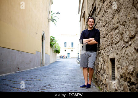 A young brunette dashing man standing in a traditional Sorrento street, Amalfi coast against an old, rustic wall Stock Photo