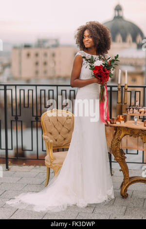 Charming black bride with wedding bouquet in hands standing on the terrace Stock Photo