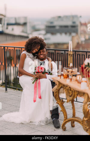Charming black wedding couple tenderly hugging on the rooftop Stock Photo