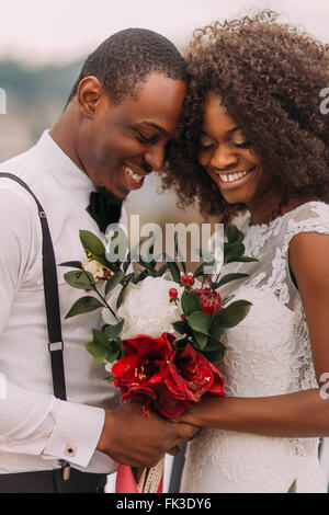 African wedding couple softly smiling with eyes closed with bouquet in hands Stock Photo