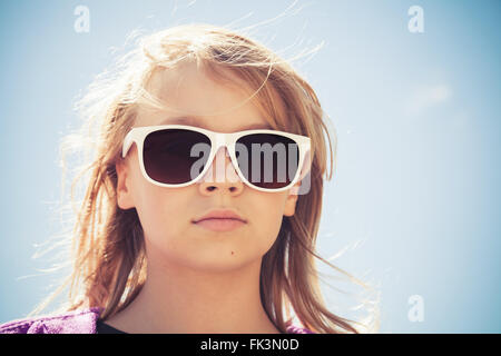Beautiful blond Caucasian girl in sunglasses, outdoor closeup portrait over blue sky background Stock Photo