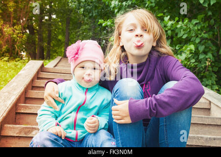 Funny little blond Caucasian sisters show tongues. Outdoor portrait with tonal correction photo filter effect Stock Photo