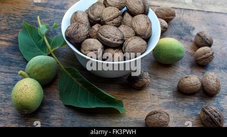 Whole, cracked and green walnuts on wooden table and in white bowl, for display. Stock Photo