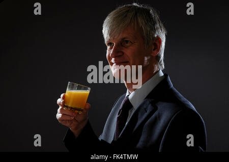 Man in business suit smiling and drinking orange juice Stock Photo