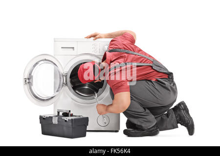 Young repairman examining a washing machine and holding a wrench isolated on white background Stock Photo