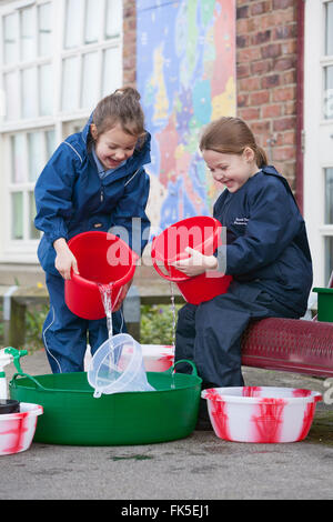 Two primary school pupils enjoying water play outside using various buckets and toys. Stock Photo