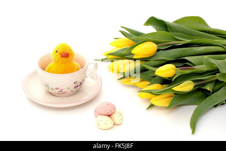 A little chicken in a cup with easter eggs and yellow tulips Stock Photo