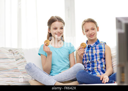 happy girls watching tv and eating cookies at home Stock Photo